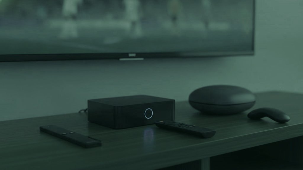 A streaming stick, a set-top box and a round streaming box with their remotes on a TV console
