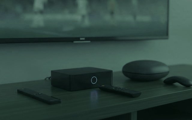 A streaming stick, a set-top box and a round streaming box with their remotes on a TV console